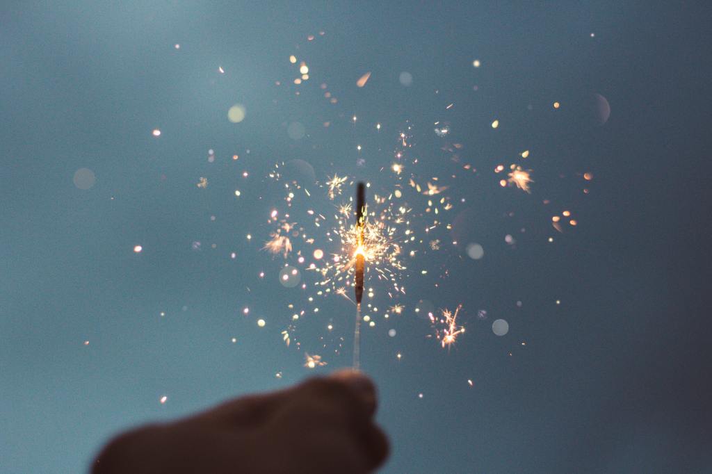 bright sparkler on a grey background, held by an unknown person.